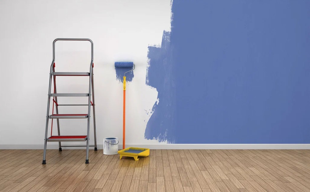 Interior painting in progress with a blue wall, paint roller, tray, and ladder in a modern room.