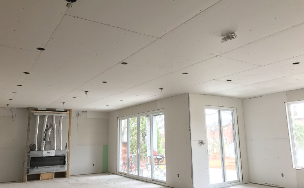 Drywall Installation in a spacious open-concept residential interior with newly hung ceiling and wall drywall panels, recessed lighting cutouts, and large patio doors.
