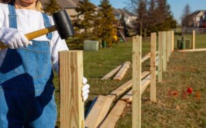 Fence Installation in progress as a person uses a rubber mallet to secure wooden fence posts in a residential backyard.