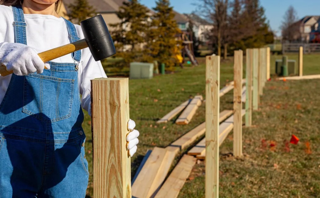 Fence Installation in progress as a person uses a rubber mallet to secure wooden fence posts in a residential backyard.