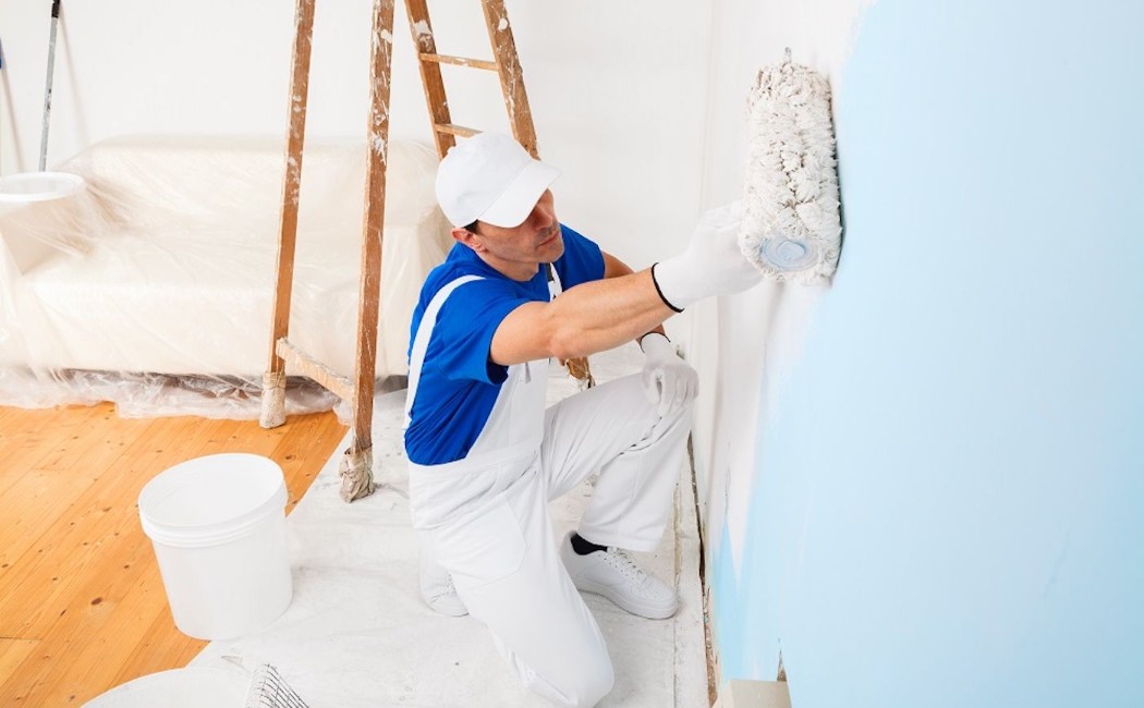 Interior painting expert applying fresh blue paint to an interior wall with a roller in a residential room during a home renovation project.