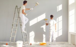 Interior Painting professionals applying fresh paint to interior walls in a bright residential room using rollers and ladders for a smooth finish.