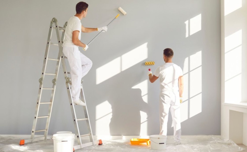 Interior Painting professionals applying fresh paint to interior walls in a bright residential room using rollers and ladders for a smooth finish.