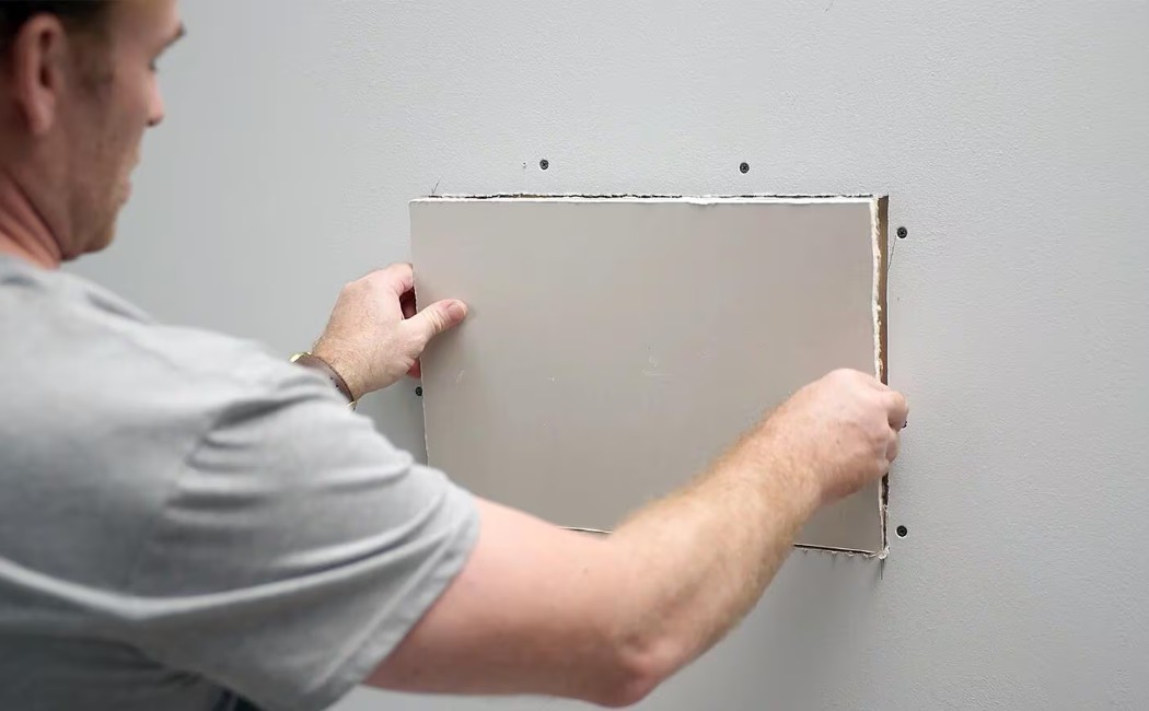Drywall Repair and Seamless Wall Restoration. Drywall Repair technician patching a damaged interior wall with a new drywall panel for seamless restoration.