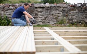 Deck Installation in progress as a worker secures decking boards onto a newly constructed wooden frame outdoors.
