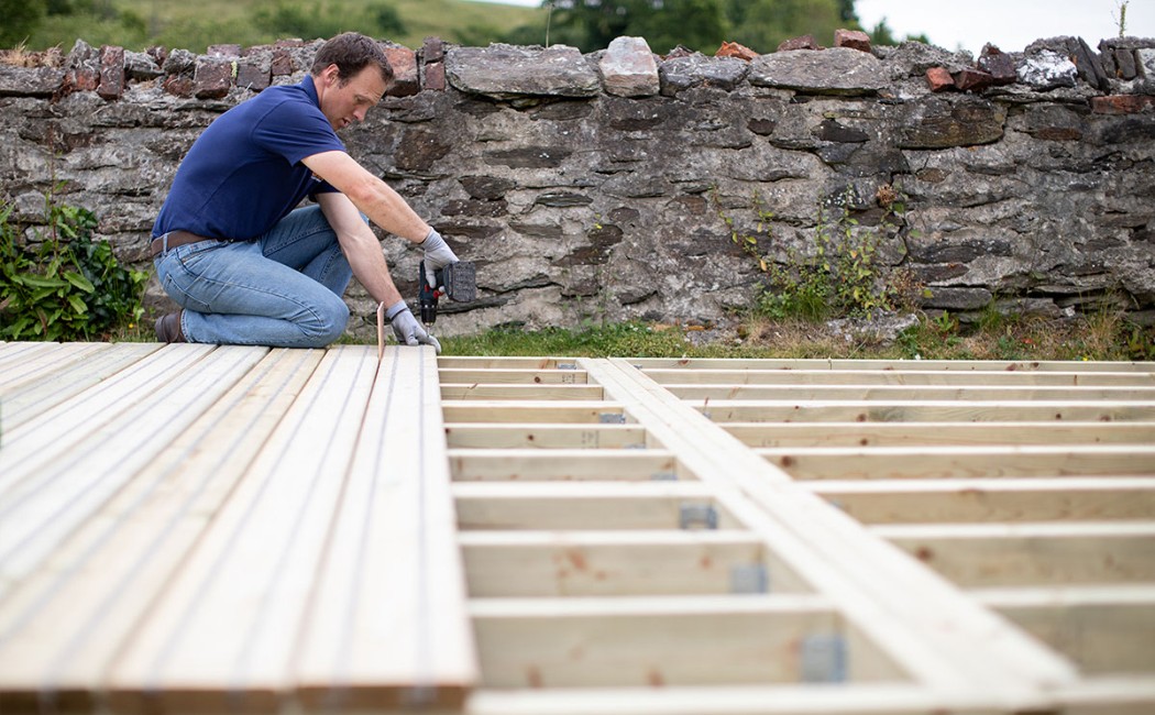 Deck Installation in progress as a worker secures decking boards onto a newly constructed wooden frame outdoors.
