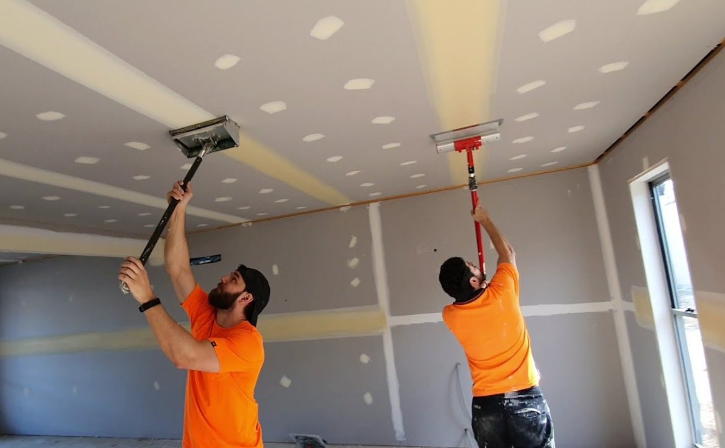 Drywall installation professionals finishing and sanding drywall ceilings and walls to create a smooth surface before painting.