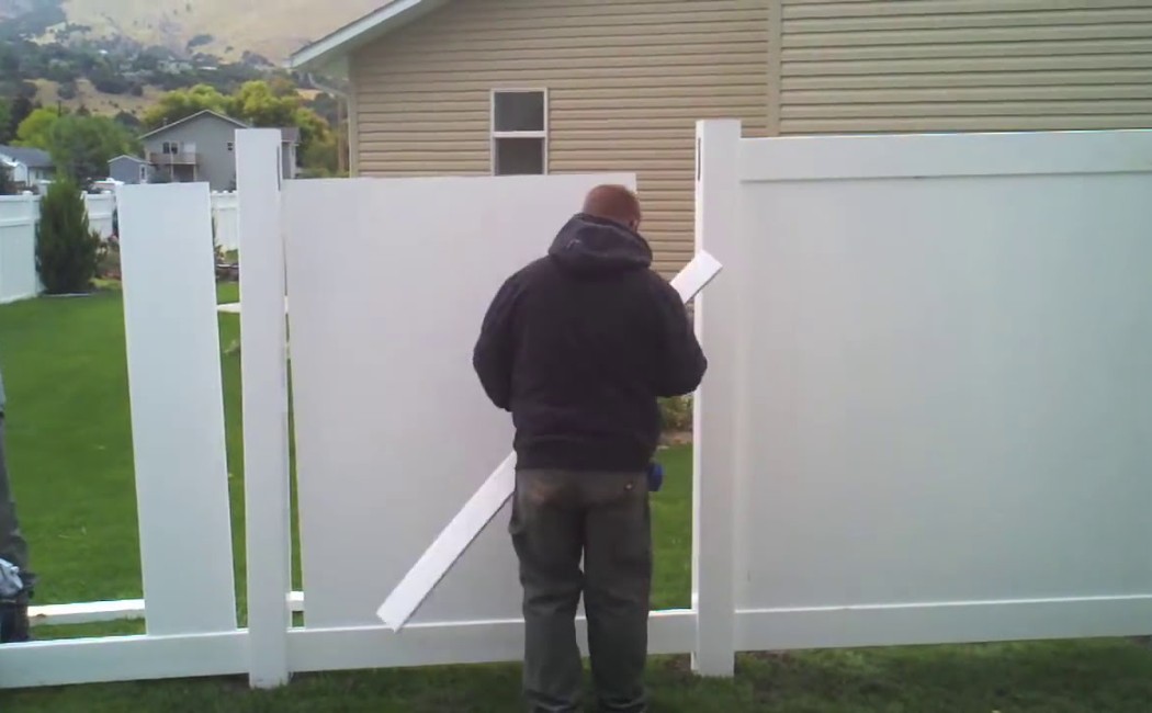 Fence Installation in progress as a worker assembles white vinyl fence panels and posts in a residential backyard.
