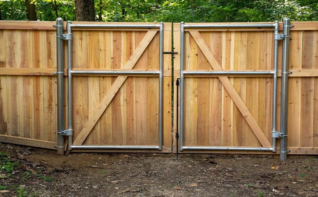 Wooden Double-Gate Fence Installation & Repair. Fence Installation & Repair services showcased with a sturdy wooden double-gate fence featuring reinforced metal framing in a residential outdoor setting.