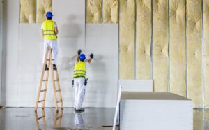 Professional drywall installation contractors installing large drywall panels on interior wall framing during a commercial construction project.
