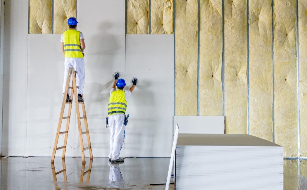 Professional drywall installation contractors installing large drywall panels on interior wall framing during a commercial construction project.