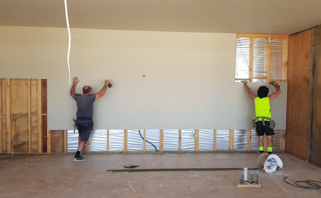 Expert Residential Drywall Installation Team. Experienced drywall installation specialists securing large drywall panels to wall framing during a residential interior construction project.